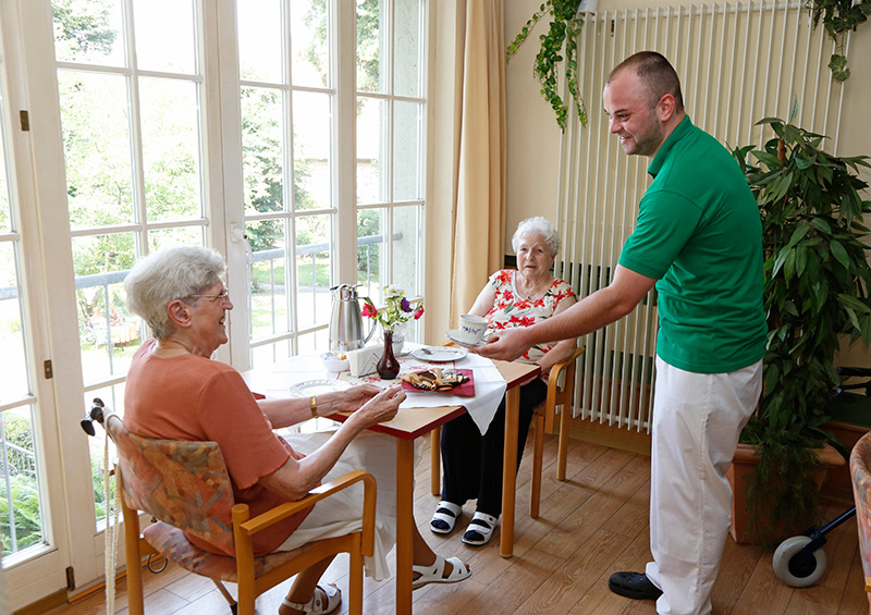 Ein Pfleger serviert einer Seniorin eine Tasse Kaffee