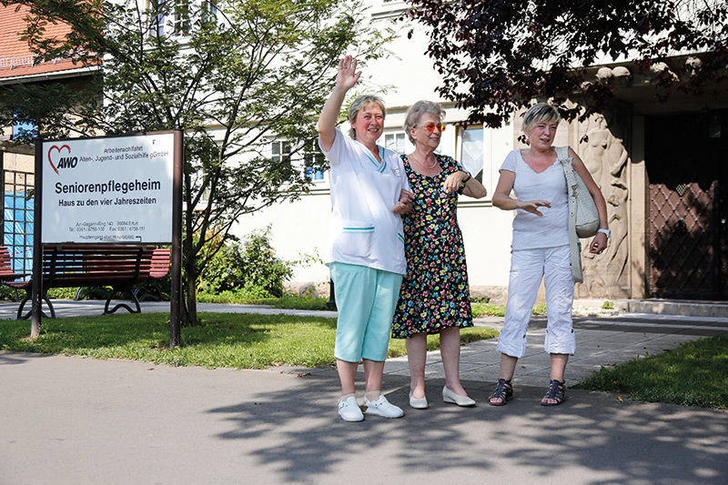 Seniorin mit Pflegekräften vor dem Haus